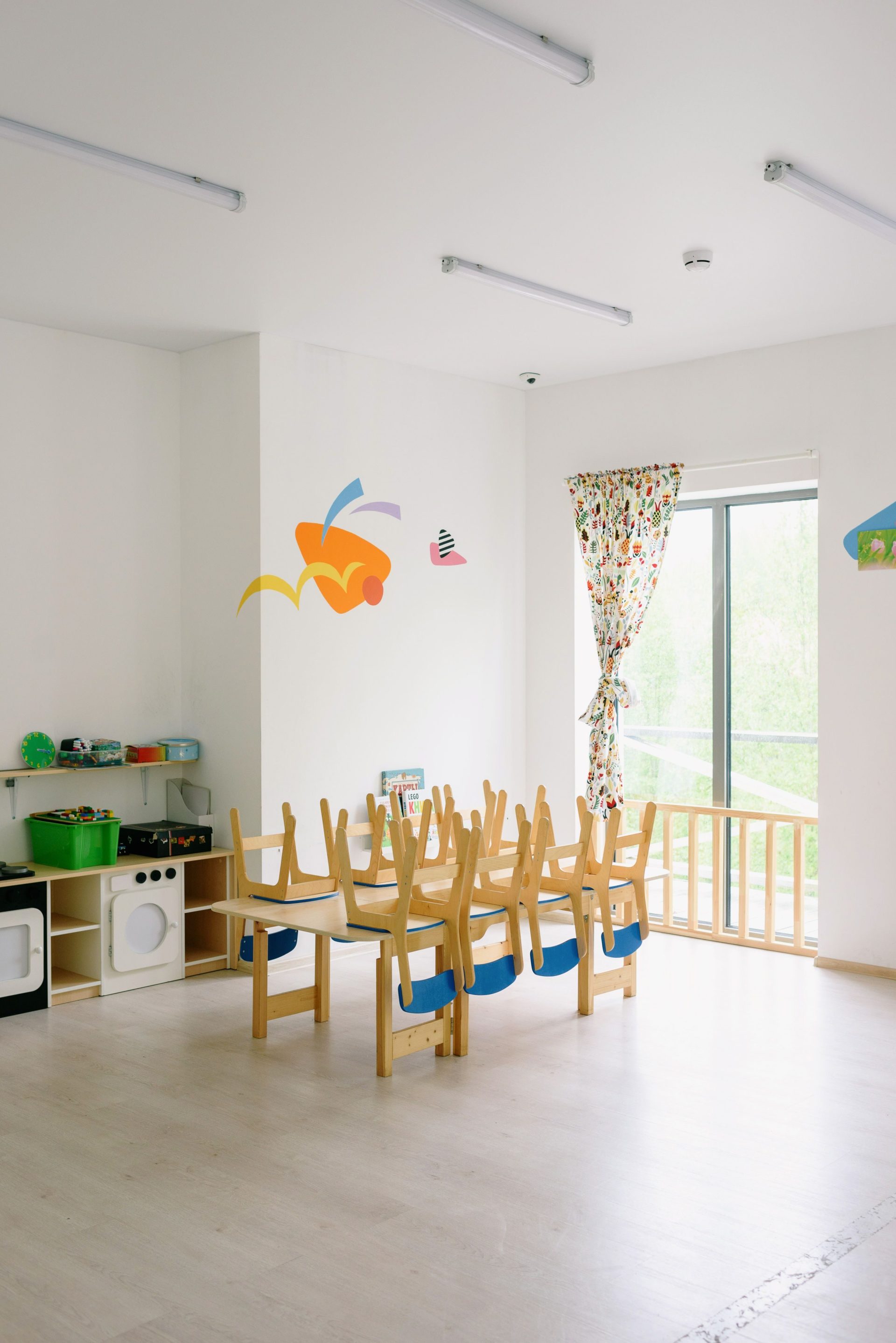 Geräumiger und heller Kindergarten-Gruppenraum mit kindgerechten Holzmöbeln und verspielter Dekoration.